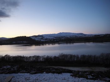 Scenic view of lake by snowcapped mountains against sky during winter