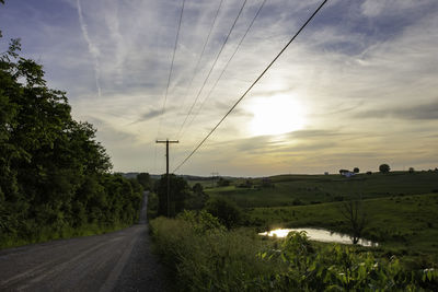 Road by trees against sky during sunset
