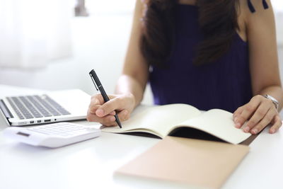 Midsection of woman writing in book at office