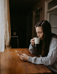 Freelance woman with the coffee and mobile phone at home thinking dee