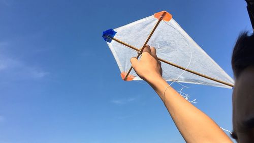 Low angle view of hands holding kite blue sky