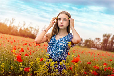 Young woman standing by poppy flowers on field against sky