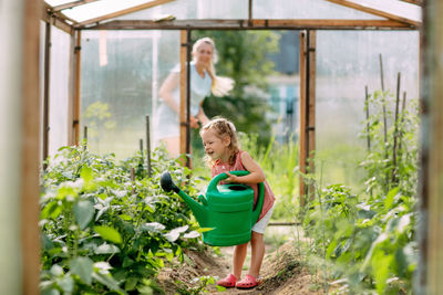 A cheerful baby with a watering can waters the plants in the greenhouse, helps to take care of them. 