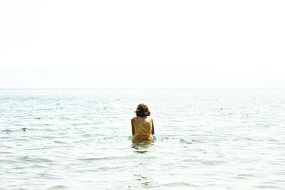 Rear view of man sitting in sea against clear sky