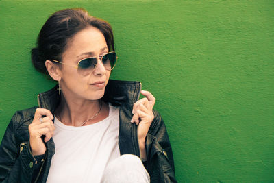  woman wearing sunglasses and leather jacket against green wall