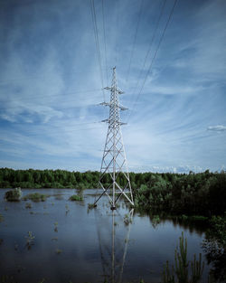 Electricity pylon by lake against sky