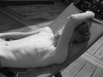 Shirtless teenage boy listening to music on headphones while lying on deck chair