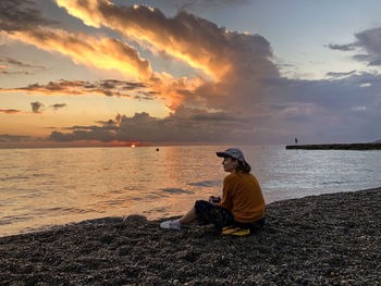 Rear view of young woman sitting on beach during sunset