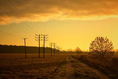 Electricity pylons on field against sky during sunset