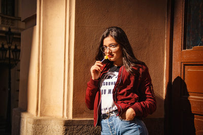 Portrait of young woman standing against wall