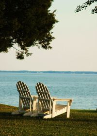 Empty chair on shore by sea against sky