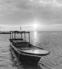 Boat moored in calm sea against cloudy sky