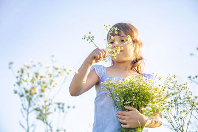 Girl with flowers standing against sky