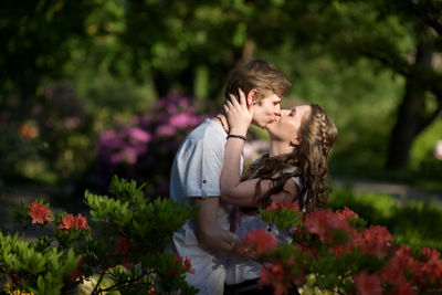 Side view of couple kissing while standing amidst flowers at park