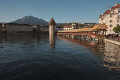 Bridge over river by buildings against clear sky