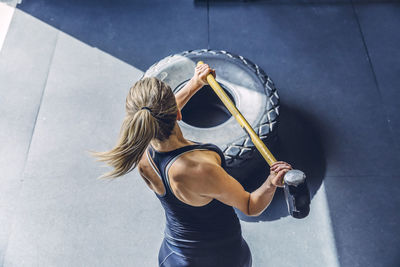 High angle view of woman hammering tire while exercising in gym