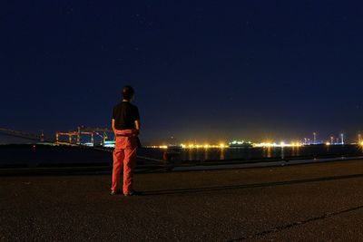 Rear view of man standing on illuminated bridge against sky at night