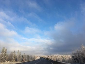 Road by trees against sky during winter