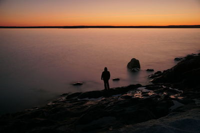 Rear view of man walking on beach against sky during sunset