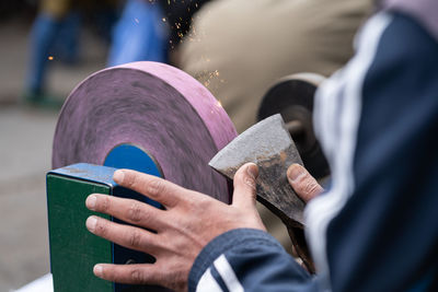 Master sharpens ax on electric sharpener with bright sparks and holds blade with his brutish fingers