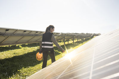 Rear view of female engineer examining solar panels at sunny day in field