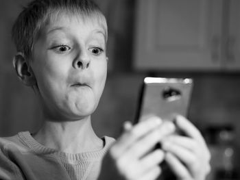 Close-up of shocked boy using phone at home