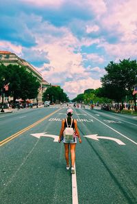 Rear view of girl walking on road against sky