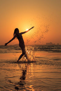 Silhouette of woman dancing in water at sunset