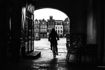 Silhouette person riding bicycle on street against buildings