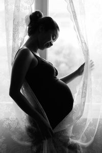 Side view of pregnant woman standing by window at home