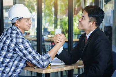 Businessman and construction worker arm wrestling on table at office