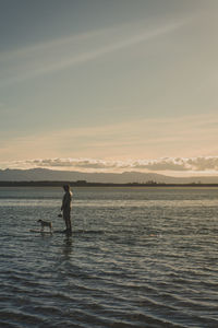 Man paddleboarding with dog in sea against sky