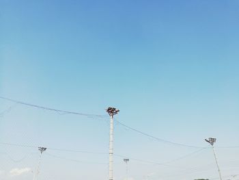 Low angle view of floodlights and netting against blue sky