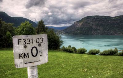 Close-up of information sign by lake against sky