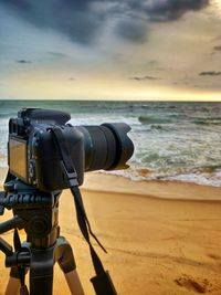 Tilt image of camera on beach against sky during sunset