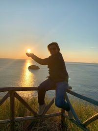 Man photographing sea against sky during sunset