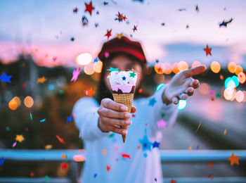 Confetti falling on woman having ice cream cone while standing in city during sunset