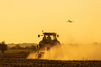 Helicopter flying over agricultural field against sky during sunset