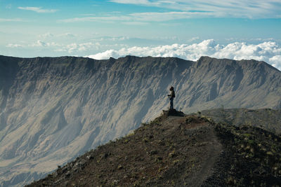 Side view of young man standing on mountain against sky