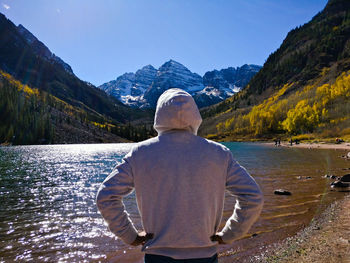 Rear view of man standing at lakeshore against mountain range