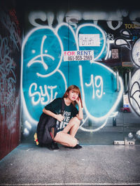 Portrait of young woman sitting against graffiti wall