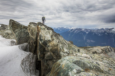 Rear view of climber standing on rocky summit ridge.