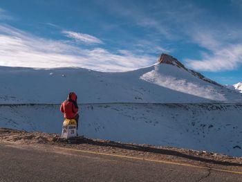 Rear view of person standing on snowcapped mountain against sky