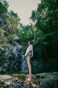 Woman standing on rock against trees in forest