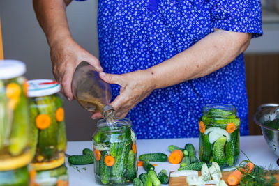 Process of canning a cucumber, senior woman canning fresh cucumbers with onion and carrots