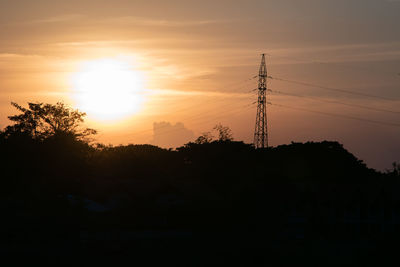 Silhouette trees and electricity pylon against sky during sunset