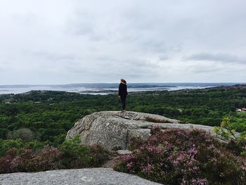 Rear view of man standing on cliff by sea against sky