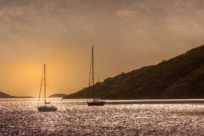 Sailboats in sea against sky during sunset