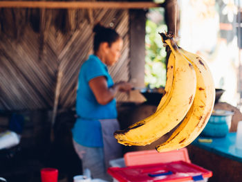 Close-up of bananas hanging with woman standing in background