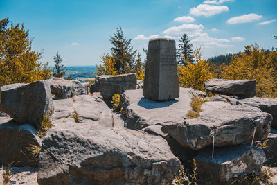 Stone wall by rocks and trees against sky